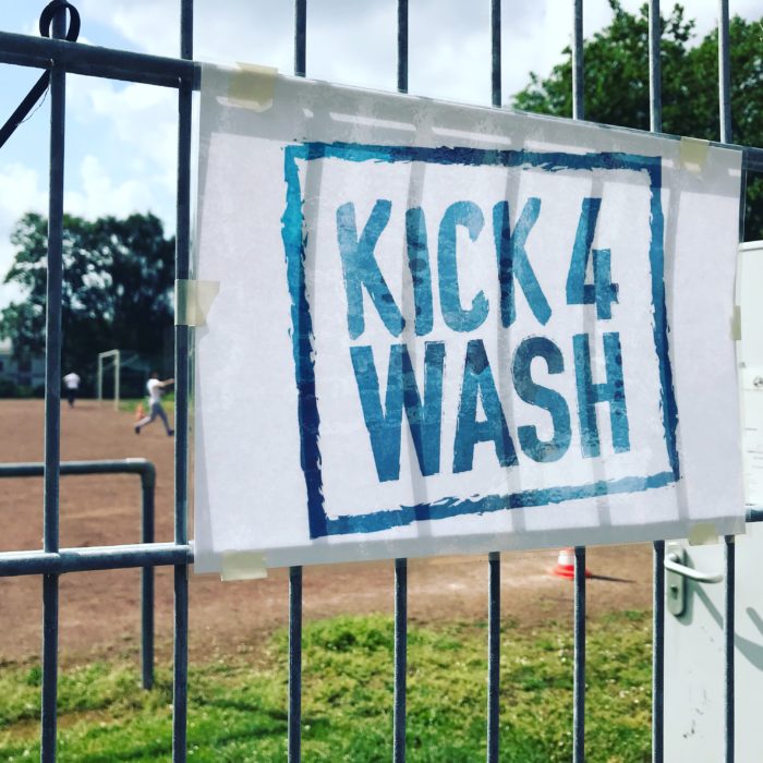 Ein Kick4Wash-Banner hängt am Zeun eines Sportplatzes