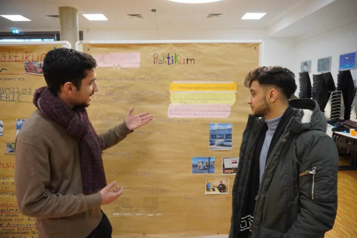 Schüler reden miteinander vor einer Metaplanwand mit einem selbstgestalteten Plakat.